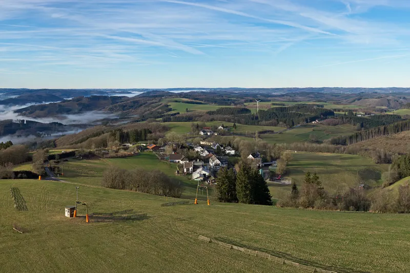 Wildewiese v kopcích Sauerlandu, s lyžařským vlekem na louce a vesnicí pod ní