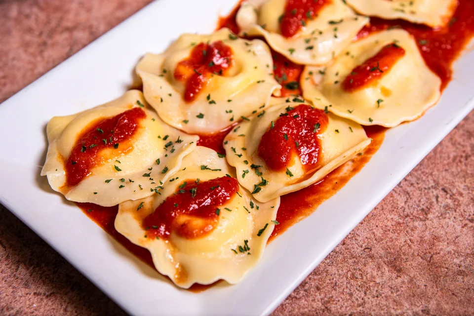 Ukázková fotografie: Ravioli s rajčatovou omáčkou a bylinkami na bílém talíři